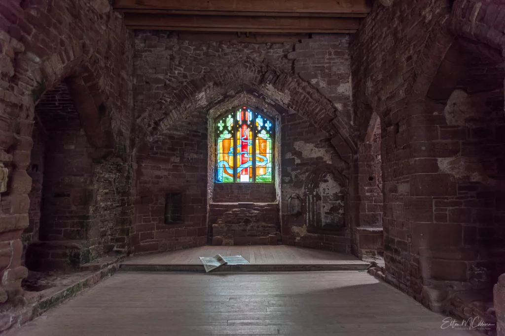 Goodrich Castle Chapel showing a stained glass window and a medieval altar